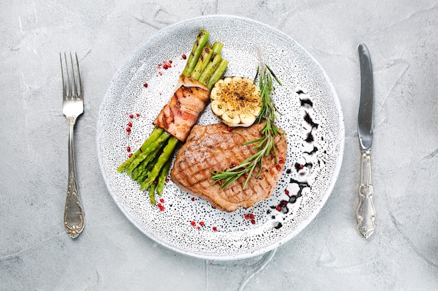 Bistecca alla griglia con asparagi e foglie di rosmarino in vista dall'alto del piatto su fondo di cemento con spazio di copia.