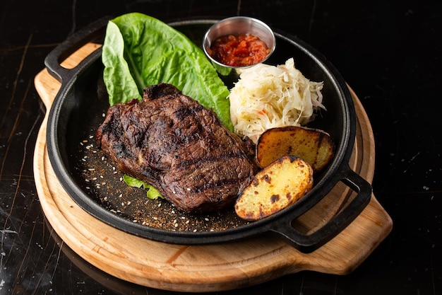 Bistecca alla griglia con patate dorate al forno servita con cavolo cappuccio e salsa rossa su fondo scuro Ricetta Deliziosa Filetto Di Maiale Cotto