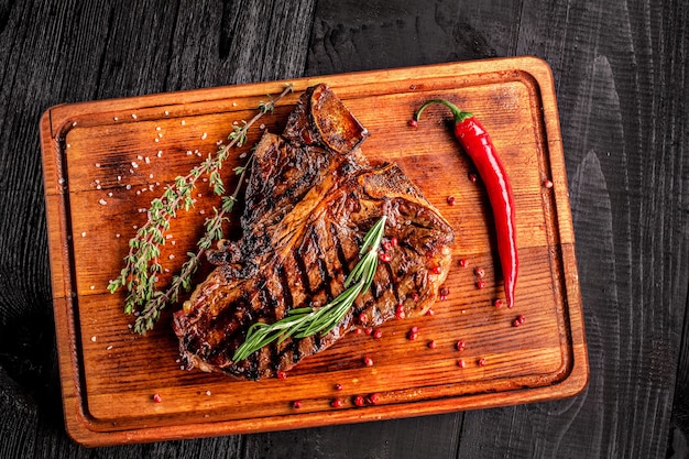 Bistecca alla griglia mediamente cotta su tagliere rustico con rosmarino e spezie sfondo rustico in legno scuro...