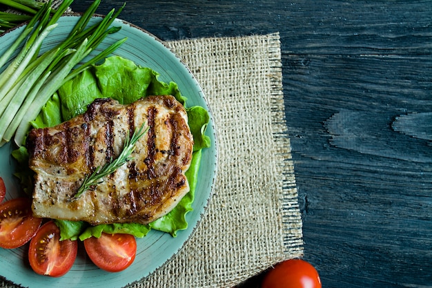 Bistecca alla griglia servita su un piatto, decorata con spezie per carne, rosmarino, verdure e verdure su un legno scuro