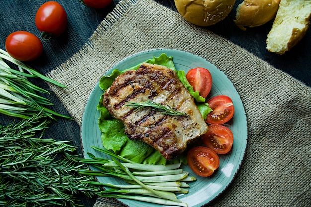 Bistecca alla griglia servita su un piatto, decorato con spezie per carne, rosmarino, verdure e verdure.