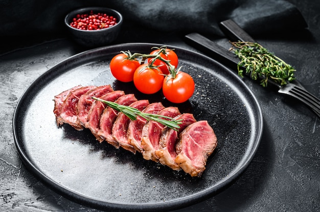 Bistecca alla griglia superiore affettata su un piatto. Carne di manzo biologica su fondo nero. Vista dall'alto