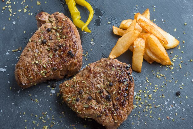 Bistecca con l'osso alla griglia condita con spezie ed erbe fresche servita su una tavola di legno con patatine fritte e peperoncini piccanti verdi