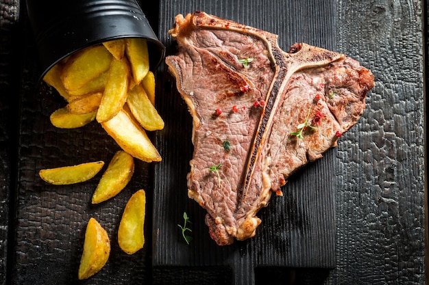 Bistecca con l'osso fatta in casa con patatine sul tavolo bruciato