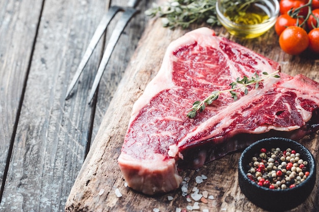 Bistecca cruda con erbe fresche e olio su fondo di legno scuro