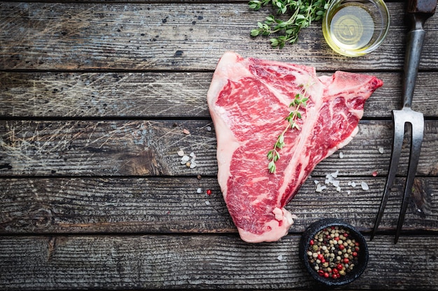 Bistecca cruda con erbe fresche e olio su sfondo di legno scuro vista dall'alto