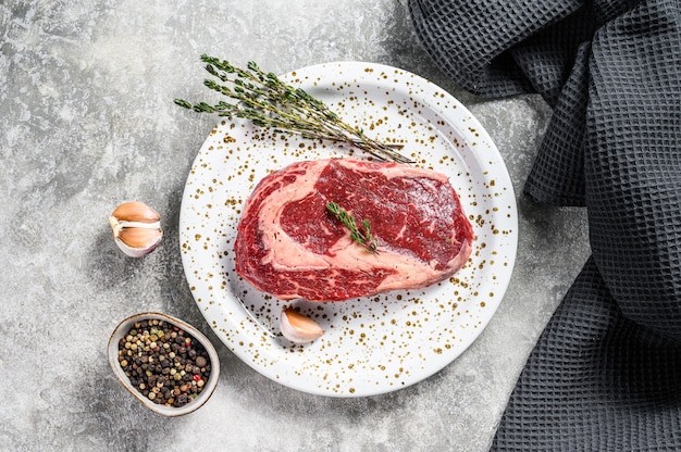 Bistecca cruda di Ribeye della carne fresca con condimento sul tagliere. Bistecca di manzo con costolette. sfondo grigio. vista dall'alto