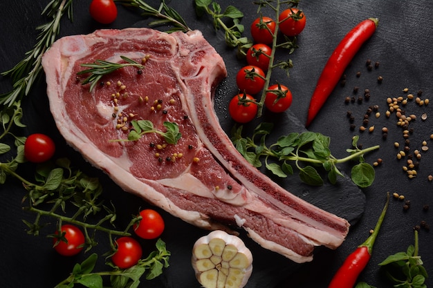 Bistecca cruda fresca della costola dell'osso del manzo sul bordo nero con le erbe e le spezie