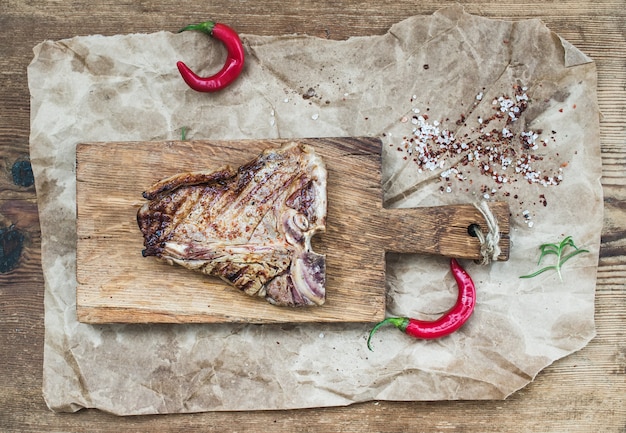 Bistecca di bistecca con l'osso cotta della carne sul bordo del servizio con i peperoncini rossi