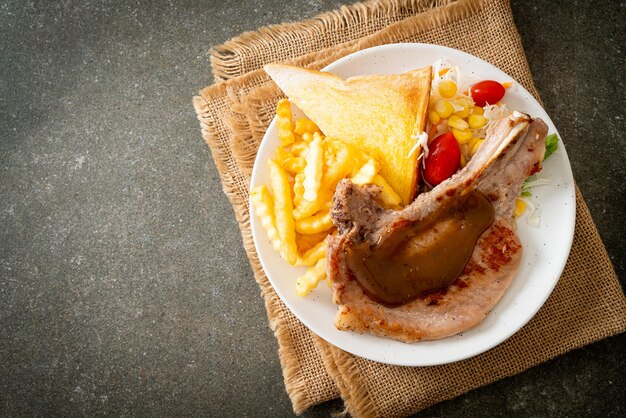 bistecca di braciola di maiale con patatine e mini insalata su piatto bianco