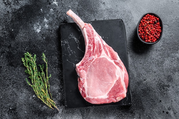 Bistecca di braciola di maiale tomahawk fresca cruda su una tavola di marmo. Sfondo nero. Vista dall'alto.