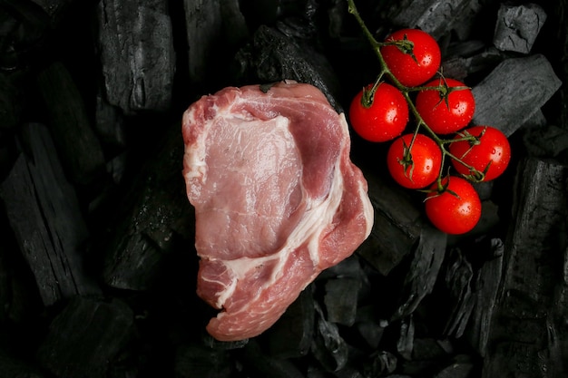 bistecca di carne cruda su uno sfondo nero di carbone bistecca cruda con pomodorini alla brace