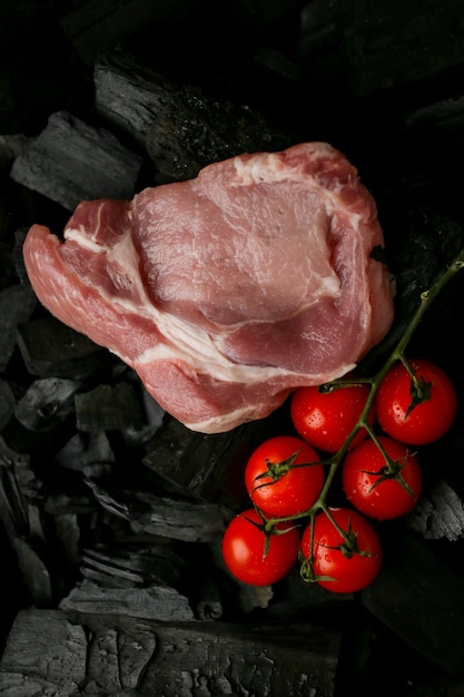 bistecca di carne cruda su uno sfondo nero di carbone bistecca cruda con pomodorini alla brace