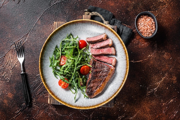 Bistecca di carne di manzo alla griglia Top controfiletto in piatto con insalata di verdure. Sfondo scuro. Vista dall'alto.