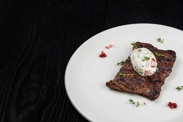 Bistecca di carne di manzo della gonna alla griglia su un piatto con salsa di verdure bianca decorata da erbe e bacche d...