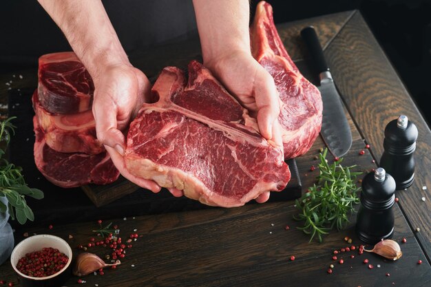 Bistecca di carne di manzo Lo chef taglia la bistecca di manzo Le mani dell'uomo tengono la bistecca cruda Tomahawk su un tagliere di legno rustico su sfondo nero Ricette di cucina e concetto di alimentazione Messa a fuoco selettiva