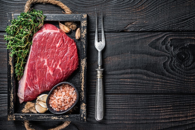 Bistecca di carne tagliata di manzo o Picanha in vassoio di legno con erbe aromatiche. Tavolo in legno nero. Vista dall'alto.