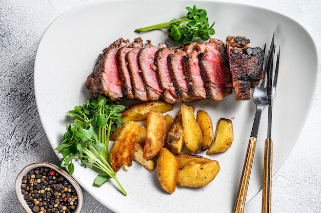 Bistecca di controfiletto a fette con patate. Sfondo bianco. Vista dall'alto.