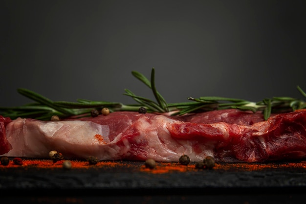 Bistecca di costata cruda con rosmarino e condimenti su una tavola di pietra nera Cibo sano Vista del profilo del primo piano Spazio per il testo