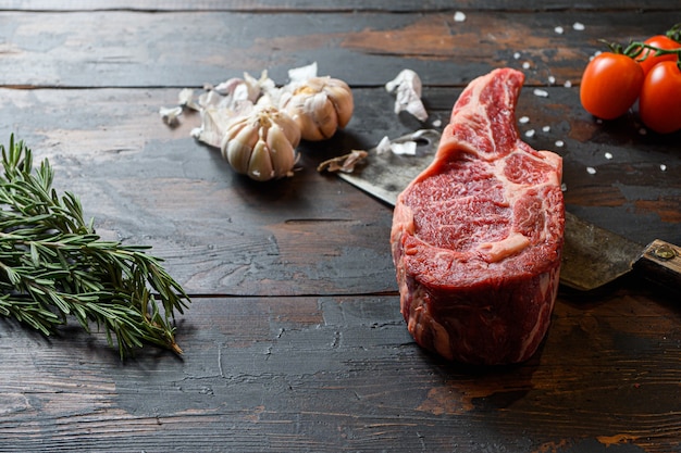 Bistecca di Dallas di manzo crudo, che si trova sul coltello da taglio. Carne di manzo cruda preparata per la cottura delle bistecche. Accanto agli ingredienti per la cottura delle bistecche, spezie ed erbe aromatiche rosmarino aglio. Vista laterale.