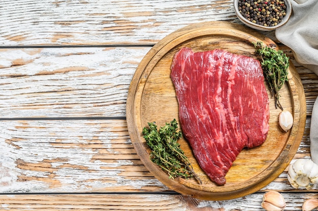 Bistecca di ferro piatto crudo su un tagliere. Carne di manzo Marmo Fresco Black Angus. Fondo in legno bianco. Vista dall'alto. Copia spazio.