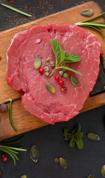 Bistecca di filetto di manzo crudo con erbe e spezie su tavola di legno su vista superiore del tavolo scuro