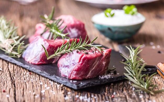 Bistecca di filetto di manzo crudo su tagliere con sale pepe rosmarino in altre posizioni