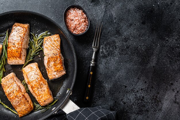 Bistecca di filetto di salmone arrosto in padella con rosmarino. Sfondo nero.