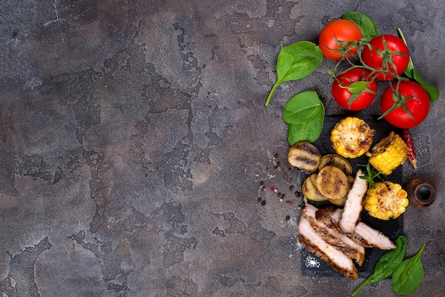 Bistecca di maiale a fette e verdure grigliate sul bordo di ardesia sul tavolo di pietra.