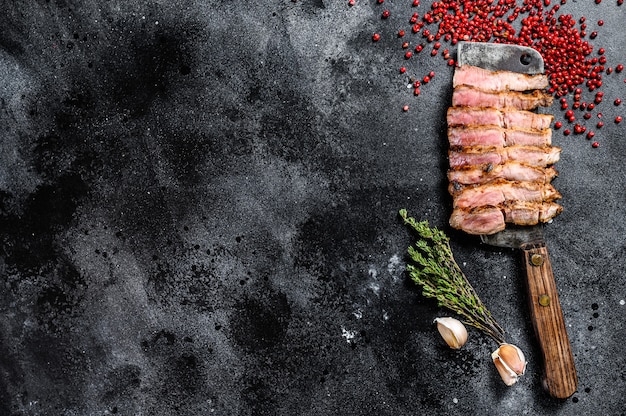 Bistecca di maiale affettata alla griglia su una mannaia di carne. Carne biologica. Sfondo nero. Vista dall'alto. Copia spazio.