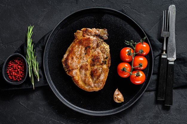 Bistecca di maiale alla griglia con pomodori. Sfondo nero. Vista dall'alto