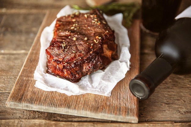 Bistecca di maiale arrosto con bottiglia di vino rosso e spezie su fondo di legno