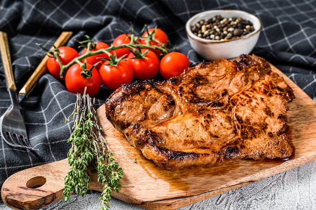 Bistecca di maiale arrosto su un tagliere. Carne biologica. Sfondo grigio.