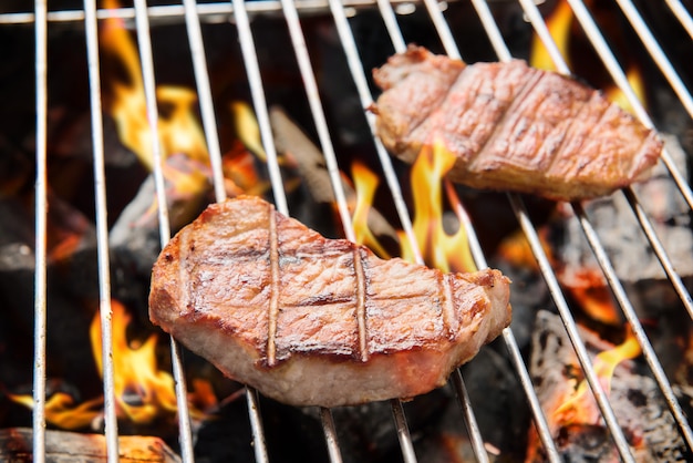 Bistecca di maiale che cucina sopra la griglia ardente.