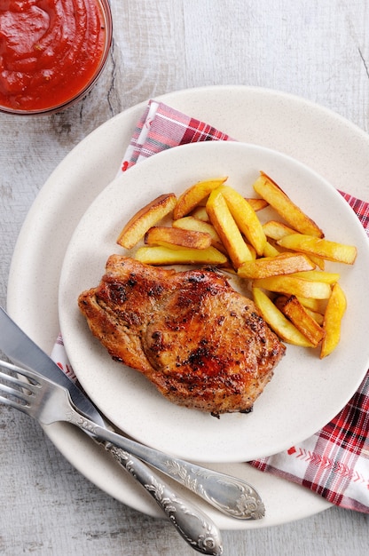 Bistecca di maiale succosa e rosolata con osso con patate fritte