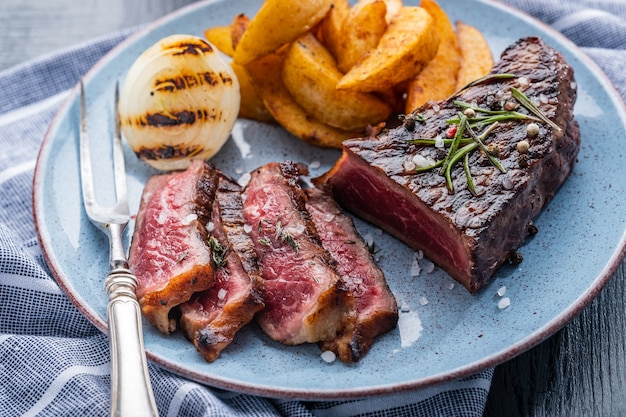 Bistecca di manzo alla griglia affettata. Bistecca di manzo media con patate e cipolla fritta