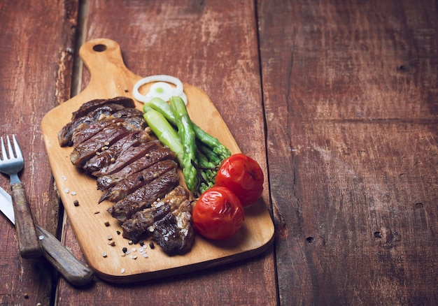 Bistecca di manzo alla griglia con asparagi e pomodori su un tavolo di legno rustico