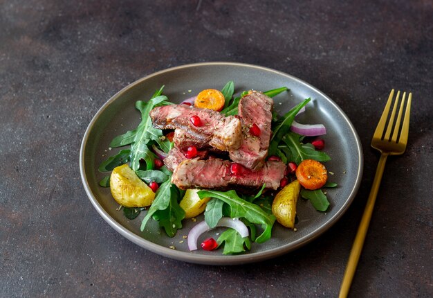 Bistecca di manzo alla griglia con insalata di rucola, patate, carote, cipolle e melograno. Mangiare sano. Dieta.