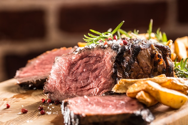 Bistecca di manzo alla griglia con patate fritte su tavola di legno.