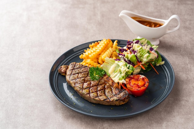 Bistecca di manzo alla griglia con patatine fritte e insalata. Servire su piatto nero. Spazio negativo.