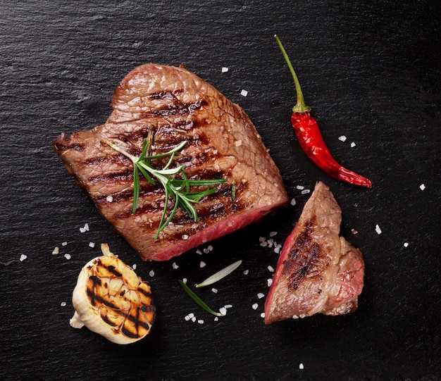 Bistecca di manzo alla griglia con rosmarino, sale e pepe su lastra di pietra nera. Vista dall'alto