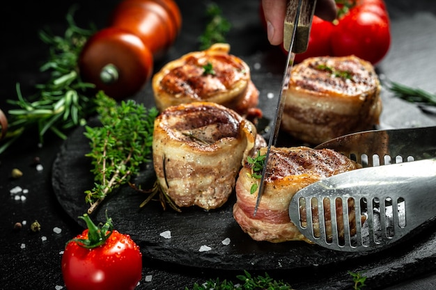 Bistecca di manzo alla griglia dalle mani dello chef su sfondo nero. filet Mignon filetto di manzo bistecca ricoperto di pancetta con spezie. vista dall'alto.