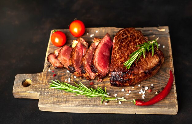 Bistecca di manzo alla griglia, erbe e spezie su un tagliere su uno sfondo di pietra, vista dall'alto