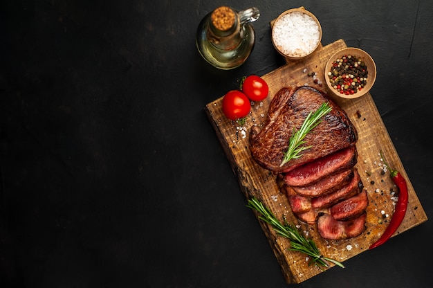 Bistecca di manzo alla griglia, erbe e spezie su un tagliere su uno sfondo di pietra, vista dall'alto