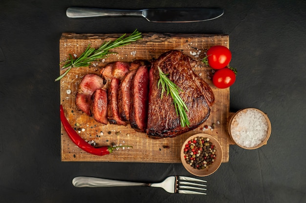 Bistecca di manzo alla griglia, erbe e spezie su un tagliere su uno sfondo di pietra, vista dall'alto