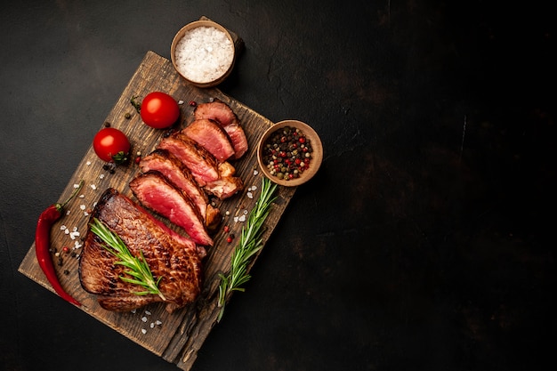 Bistecca di manzo alla griglia, erbe e spezie su uno sfondo di pietra, vista dall'alto con spazio di copia per il testo.