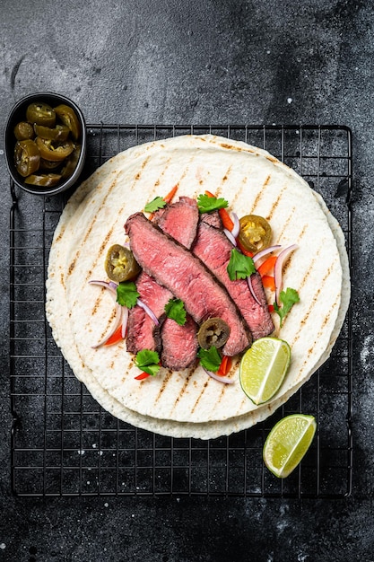 Bistecca di manzo alla griglia Fajitas taco tortillas con cipolla jalapeno e peperone Sfondo nero vista dall'alto