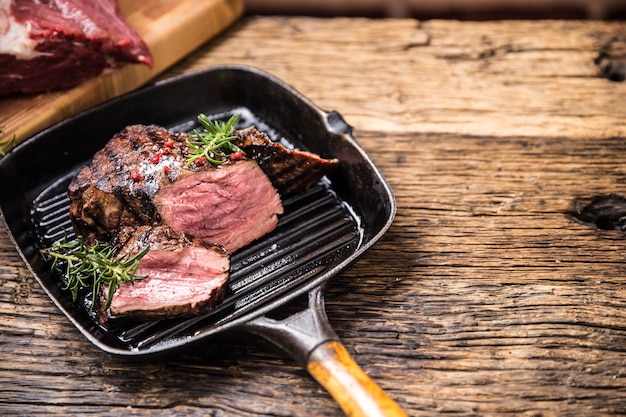 Bistecca di manzo alla griglia in padella con rosmarino erbe sul tavolo di legno.