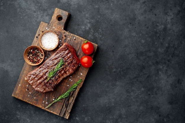 bistecca di manzo alla griglia su una tavola di legno con spezie su uno sfondo di pietra con copia spazio per il testo