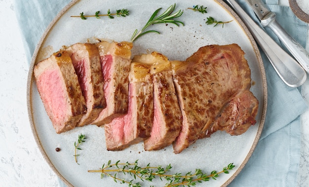 Bistecca di manzo chetogenica di dieta cheto, striploin sul piatto grigio su bianco.